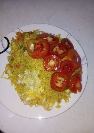 A picture of Jollof indomie and egg with sliced tomatoes.