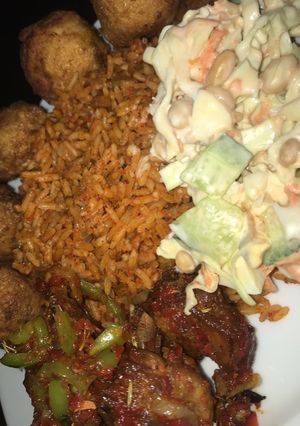 A picture of Jollof rice with salad and peppered chicken.