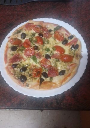 Una foto de Pizza de rúcula, jamón serrano, aceitunas negras y tomates cherry macerados