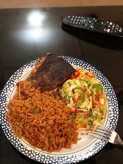 A picture of Jollof rice, fresh veggie salad with Salmon.