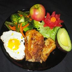 A picture of Fish fillet and a perfect over well egg garnished with tomato.
