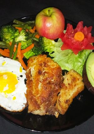 A picture of Fish fillet and a perfect over well egg garnished with tomato.
