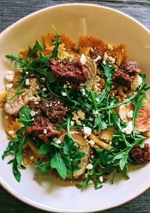 A picture of Farfalle with tomato pesto cream, beets, aragula, beyond meat.