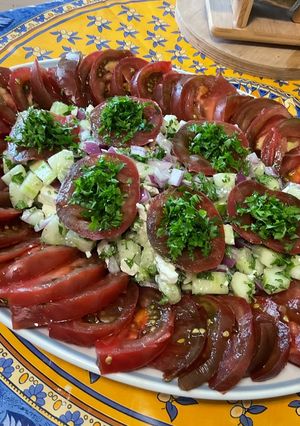 Une photo de Salade composée de tomates noires, concombre, oignon rouge, feta et persil