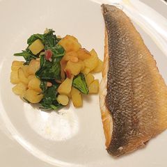 A picture of Pan fried sea bass with potatoes, spinach and toasted pine nuts.