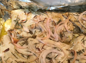 Una foto de Pescado Corvina Acostada en cama de Papas y arropada con aros de Cebolla