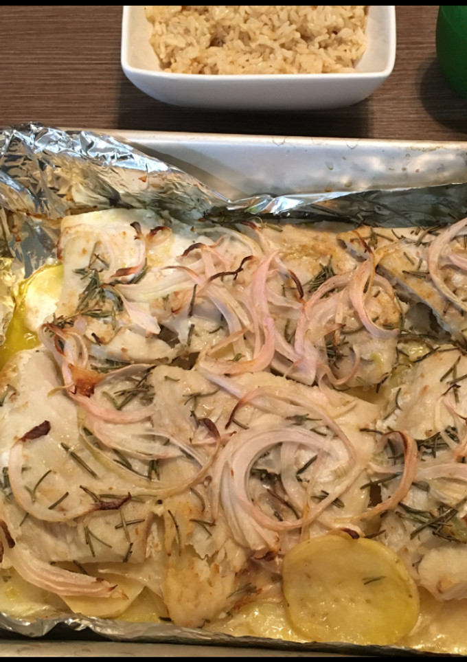 Una foto de Pescado Corvina Acostada en cama de Papas y arropada con aros de Cebolla