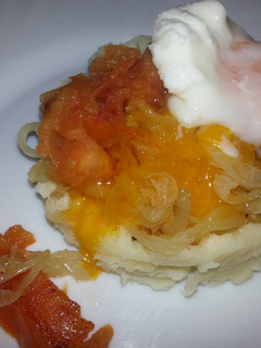 Una foto de Huevos escalfados sobre una base de patatas, cebolla y tomate