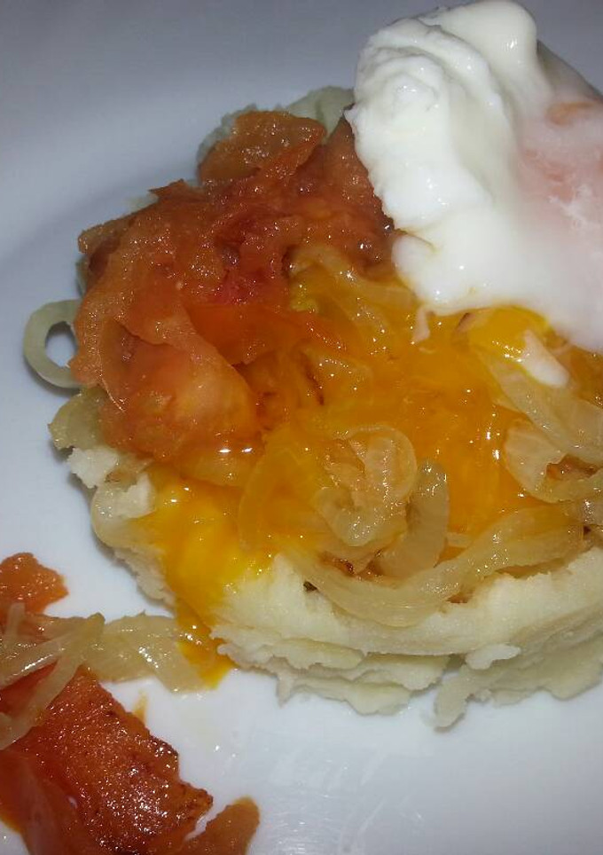 Una foto de Huevos escalfados sobre una base de patatas, cebolla y tomate