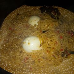 A picture of Indomie jellof with boiled egg and fry meat.