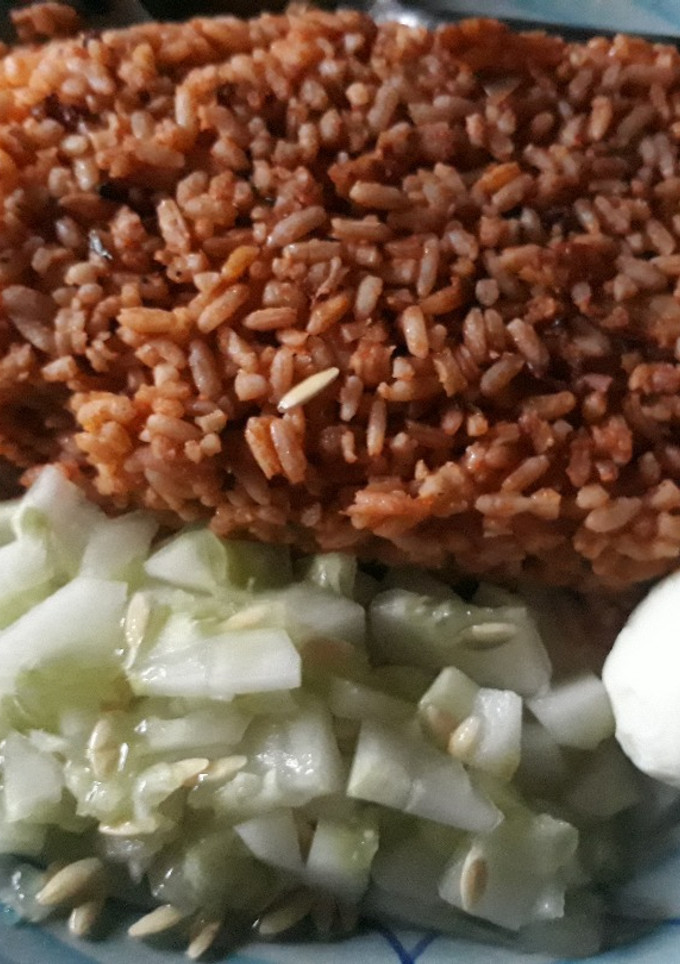 A picture of Jollof rice with cucumber and egg.