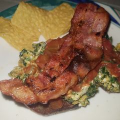 A picture of Spinach and egg scramble on rye bread, topped with crispy bacon.