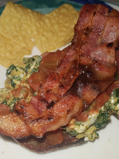 A picture of Spinach and egg scramble on rye bread, topped with crispy bacon.