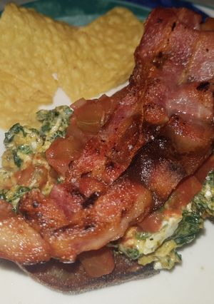 A picture of Spinach and egg scramble on rye bread, topped with crispy bacon.
