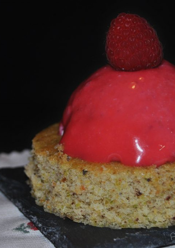 Una foto de Semiesferas de frutos rojos con glaseado espejo sobre bizcocho de pistacho