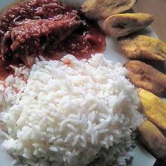 A picture of White rice with fish stew garnished with fried plantain.