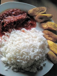 A picture of White rice with fish stew garnished with fried plantain.