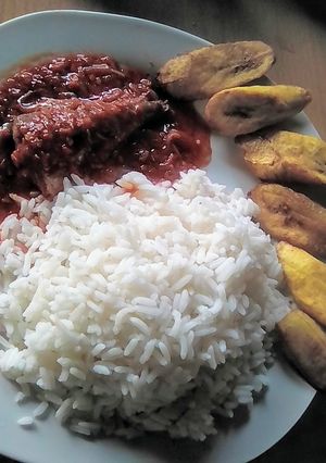 A picture of White rice with fish stew garnished with fried plantain.