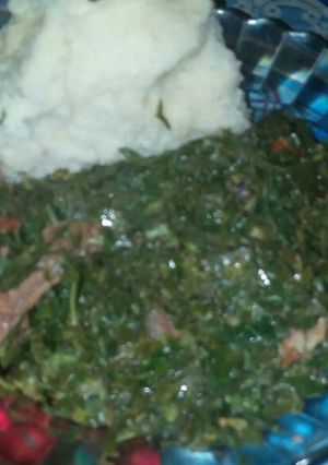 A picture of Green mixed up with red meat and ugali.