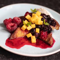 A picture of French toast with raspberry and blueberry compote and fresh mango.