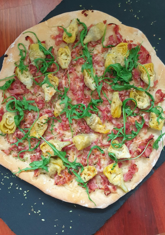 Una foto de Pizza de alcachofas, jamón y rúcula
