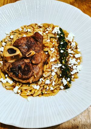 A picture of Pork osso buco, saffron orzo, tangerine gremolata and feta.