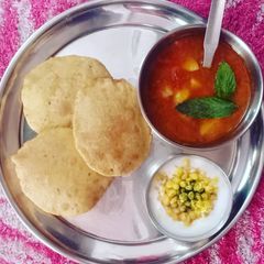 A picture of Potato Mint Tomato Curry with Puri & Boondi Raita.