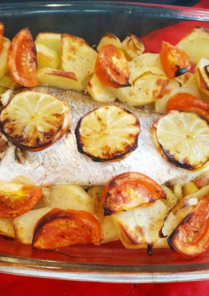 Una foto de Lubina al horno con patatas, tomates y ajos laminados