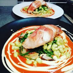 A picture of Monkfish wraped in parma ham with tomato and hummous sauce.
