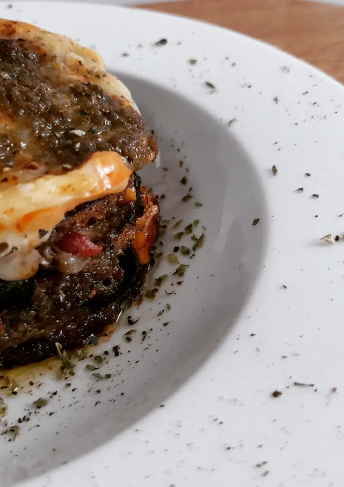 Una foto de Milhojas de berenjena empanada, puttanesca gratinada con pesto
