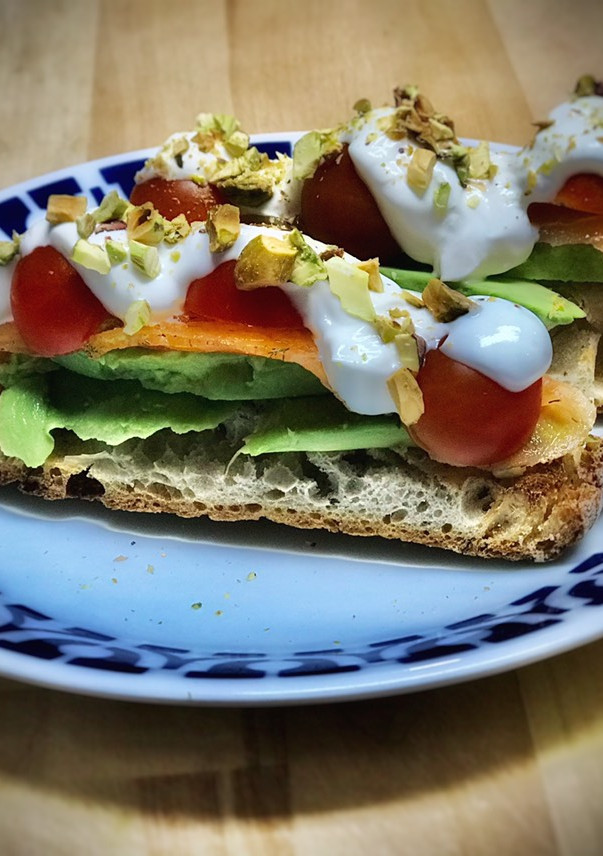 Una foto de Tosta de aguacate, salmón marinado, tomate, yogur y pistachos