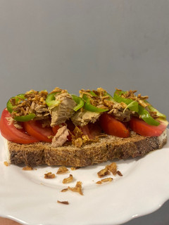 Una foto de Tostada de tomate, bonito, pimiento verde, cebolla crujiente y aove