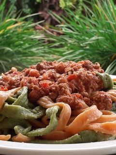Una foto de Fideos caseros de morrón y de espinaca con salsa bolognesa