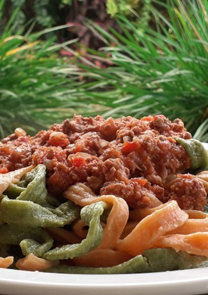 Una foto de Fideos caseros de morrón y de espinaca con salsa bolognesa