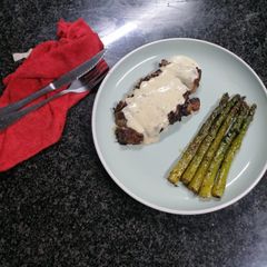 A picture of Sirloin steak and goat cheese sauce served with asparagus.