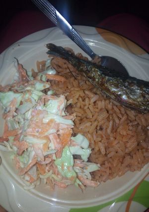 A picture of Jollof rice with fried fish and coleslaw.