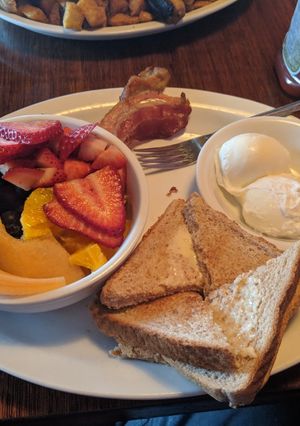 A picture of Poached eggs, bacon, toast and a bowl of fruit.