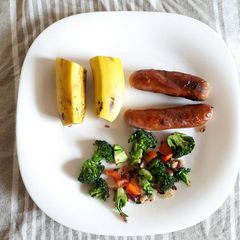 A picture of Sausages served with brocolli and fruit.