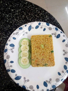 A picture of Jollof rice served with cucumber and banana.