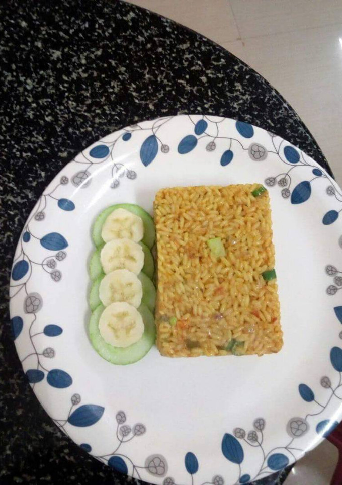 A picture of Jollof rice served with cucumber and banana.