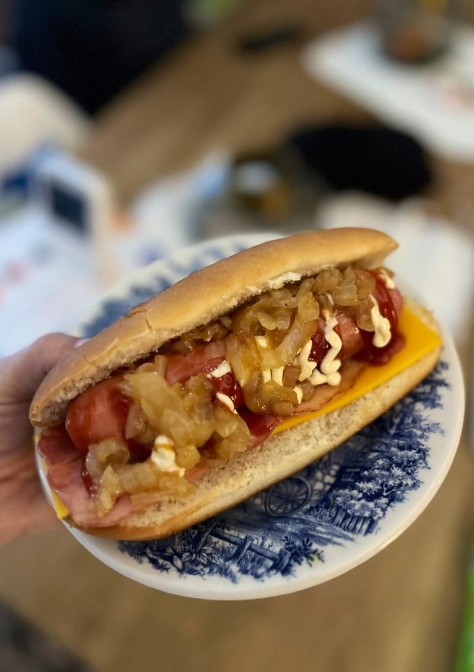 Una foto de Perrito caliente con cebolla caramelizada, bacon y cheddar