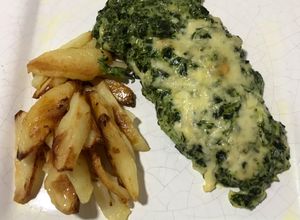 Una foto de Mila de pollo con salsa blanca y espinaca acompañado de papas al horno