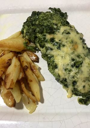 Una foto de Mila de pollo con salsa blanca y espinaca acompañado de papas al horno