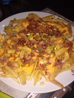 Una foto de Papas fritas con cheddar, panceta y verdeo