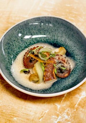 Foto di Polpo rosticciato marinato alla birra, crema di topinambur pack choi, olio verde e aglio nero
