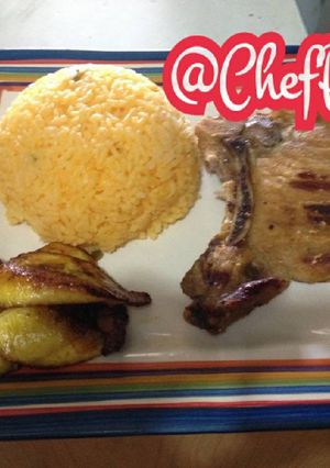 Una foto de Chuletas a la plancha con arroz amarillo con cebollas y ají acompañado de tajadas