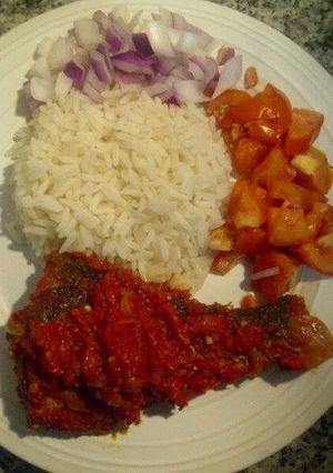 A picture of Pepper fried fish with boiled rice and sliced tomatoes.