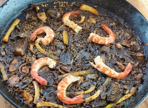 Una foto de Arroz negro de sepia, alcachofas, gambones y ajos tiernos
