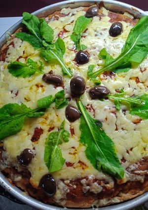 Una foto de Muzzarella integral con rúcula y aceitunas negras y parmesano🍕