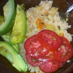 A picture of Carrot rice with avocado and fresh tomatoes.